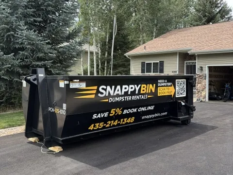 Black Snappy Bin dumpster resting on protective wooden blocks in a residential driveway