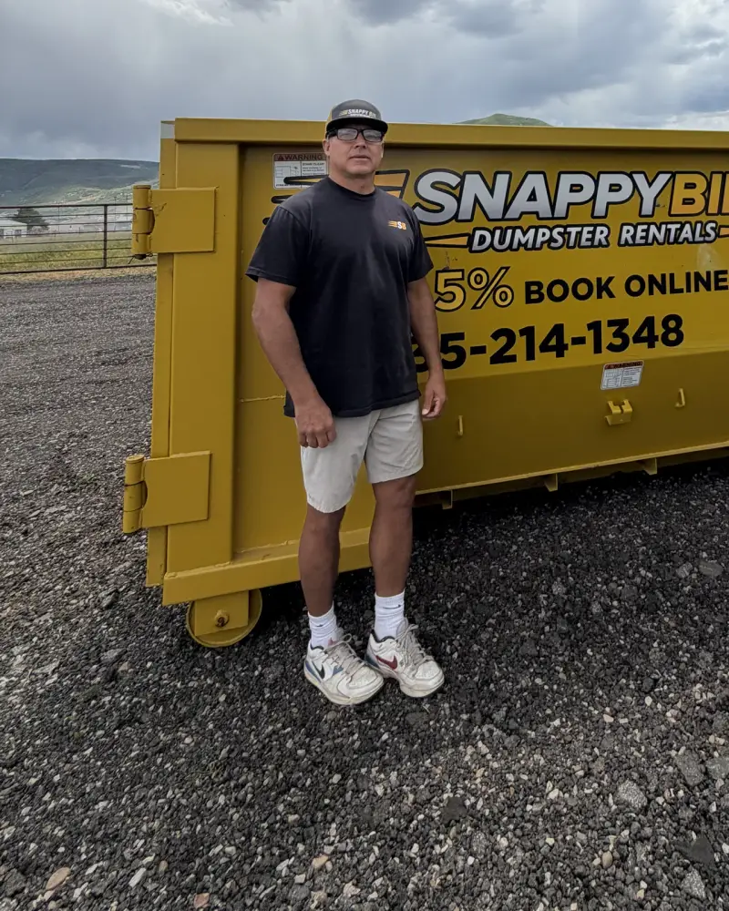 Mike Vleck, founder and owner of Snappy Bin Dumpster Rentals, beside a yellow roll-off dumpster in Park City, UT